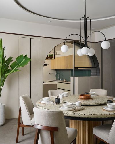 Round terrazzo dining table under sculptural globe chandelier, seen through an arched metal-framed opening to the kitchen.