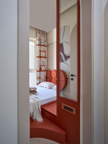 View through arched terracotta doorway into small bedroom with scalloped headboard and mirrored panel