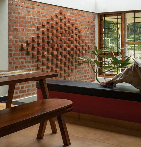 Textured red brick wall with protruding bricks above a built-in bench, wooden furniture in foreground