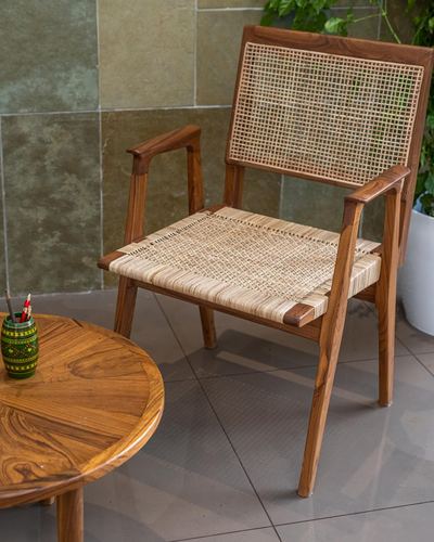 Teak armchair with cane weave beside round wooden table on tiled balcony