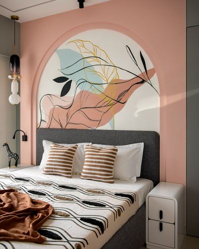 Pink bedroom with arched leaf mural above grey upholstered bed and patterned bedding