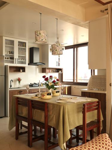 Kitchen-dining space with floral pendant lamps over a table dressed in checkered cloth, wooden chairs and cabinetry