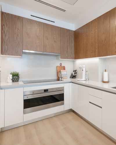 Modern L-shaped kitchen with wood-grain upper cabinets, white lower cabinetry, and integrated oven