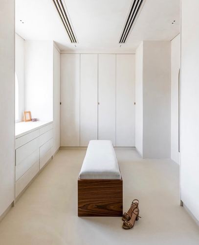 Minimalist dressing room with white wardrobes, a wood-base bench, and heels on stone floor