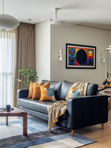 Living room with black leather sofa, mustard cushions, colorful artwork, and mid-century pendant lamp