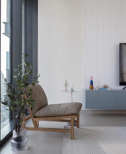 Minimalist living room corner with wood-framed lounge chair, fluted wall panel and floating blue console beneath a mounted TV