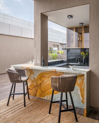 Outdoor bar counter with dramatic stone waterfall edge, rattan stools, and kitchen beyond