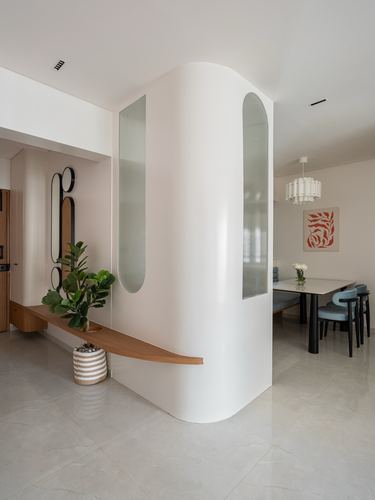 Curved white plaster partition with glass strips dividing foyer from dining area in a Pune apartment