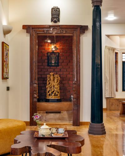 Carved wooden temple archway with brass idol against exposed brick wall in a Goan home