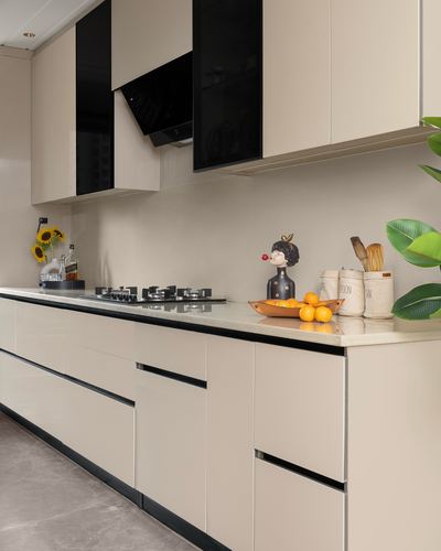 Beige modular kitchen with black chimney hood, gas hob, and styled countertop décor