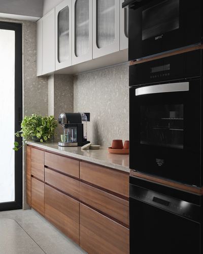 Kitchen with walnut cabinetry, terrazzo backsplash, and stacked black built-in ovens