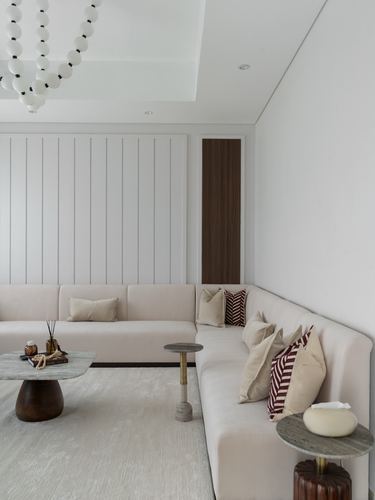 Beige sectional sofa with maroon patterned pillows beneath slatted wall panel and beaded chandelier