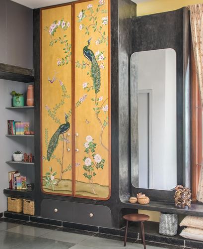 Mustard hand-painted peacock wardrobe beside black-framed mirror in a foyer with shelving