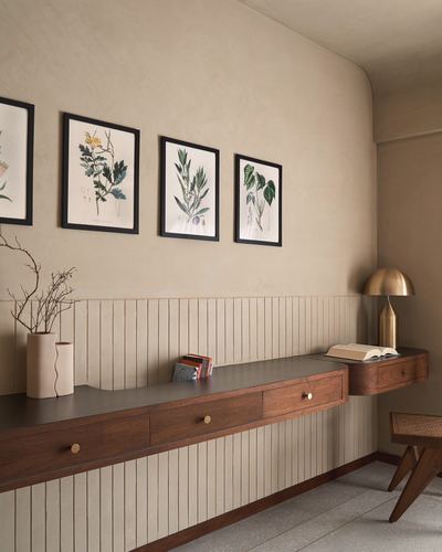 Wood console with brass drawer pulls beneath framed botanical prints on a fluted, beige plastered wall