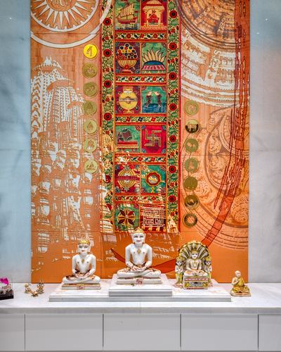 Marble Jain idols on white counter before an orange temple-motif mural in Ahmedabad home