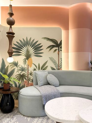 Curved sage green sofa against a tropical palm mural with a turned wood pendant light
