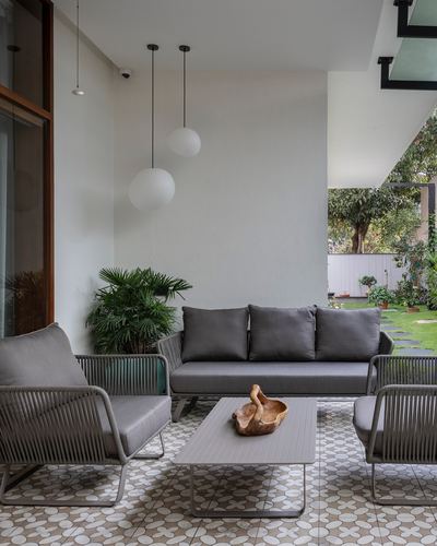 Covered patio with grey rope-and-cushion sofa set, patterned floor tile, globe pendants, and garden view beyond.