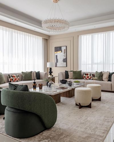 Beige living room with green sofas, curved chair, marble coffee table and crystal chandelier