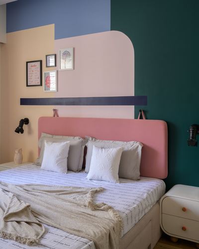 Bed with pink upholstered headboard against a color-blocked wall in teal, blue, peach and pink