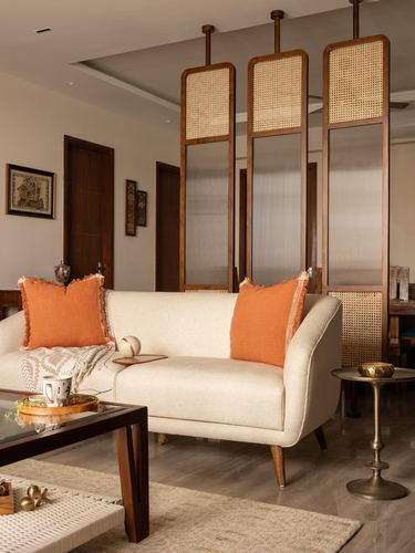 Cream sofa with orange fringed cushions beneath hanging cane room-divider panels