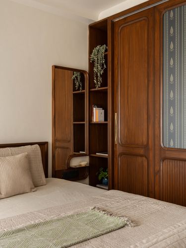 Teak wardrobe with fluted panels and arched mirror shelving beside a bed with cream linens and green throw.
