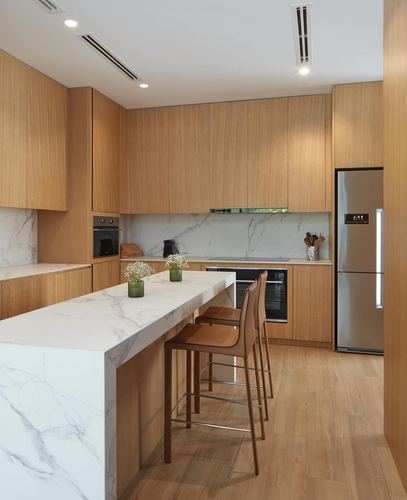 Modern wood kitchen with white stone island, waterfall edge, and stainless refrigerator