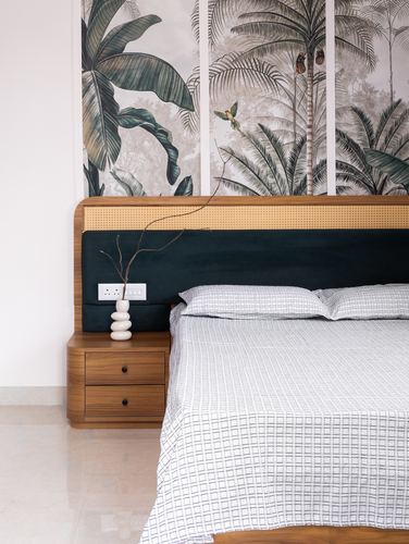 Bed with teal velvet and cane headboard against tropical leaf mural, wooden bedside table