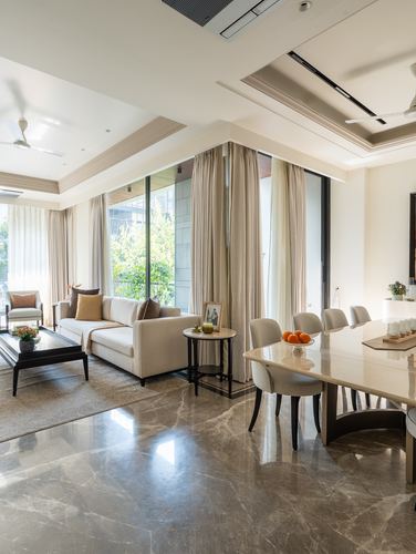 Open-plan living and dining room with beige sofa, marble floor, and floor-to-ceiling curtains, Delhi apartment