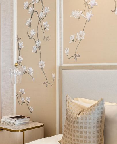 Beige upholstered headboard beside hand-painted magnolia wallpaper panels and a glass pendant light
