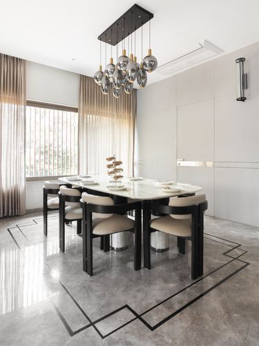 Oval marble dining table with black chairs under a cluster of pendant lights