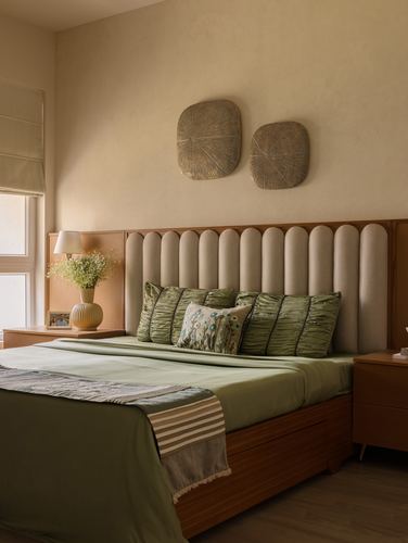 Bedroom with tall channel-tufted beige headboard, olive green bedding, and two carved wall discs above.