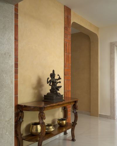 Carved wooden console with bronze idol and brass urlis beneath a brick-trimmed arched doorway