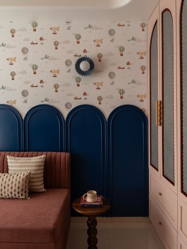 Navy arched wall panels below balloon-print wallpaper, rose sofa, cane-front wardrobe in a children's bedroom corner