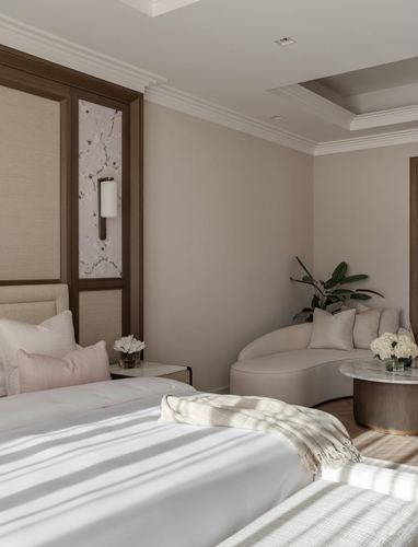 Neutral hotel-style bedroom with upholstered headboard, curved sofa, and layered moulded ceiling
