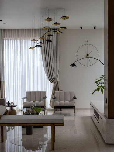Living room with striped curtains, cane armchairs, glass table and sculptural pendant lights over marble floor