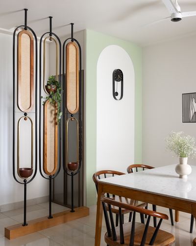 Cane and metal room divider beside mint arched niche with clock, dining table in foreground
