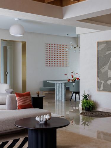 Open living-dining space with marble table, boucle sofa, and textured wall art under sculptural pendant lights