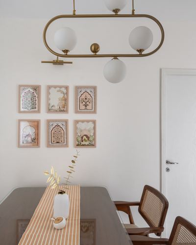 Dining table with striped runner and vase beneath a gallery wall and brass globe chandelier