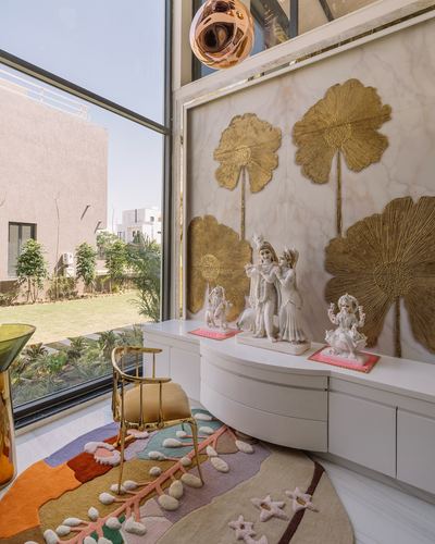 Pooja corner with marble deity idols against gold lotus wall panel beside floor-to-ceiling glass