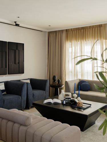 Living room with navy armchairs, beige sofa, black coffee table, and sheer curtained window