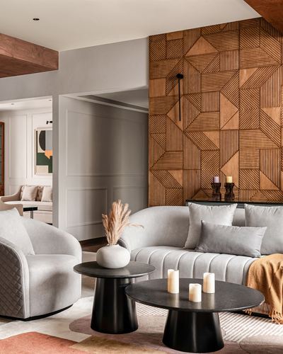 Living room with grey sofa, black round tables, and geometric wood panel wall