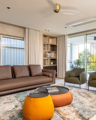 Warm-toned living room with brown leather sofa, orange round ottomans, olive armchairs and a wooden display niche.