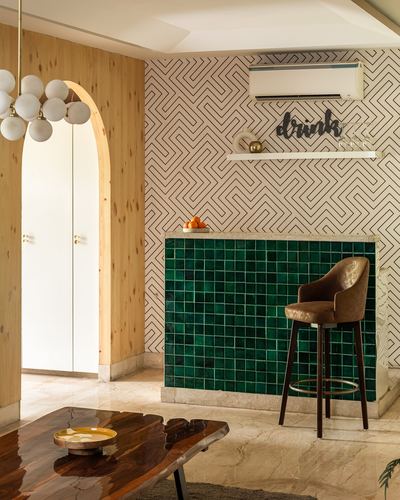 Home bar with green glazed tiles, patterned wallpaper, and a leather stool beside an arched wood-clad doorway