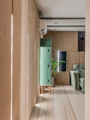 Corridor with textured beige wall, mint cabinet on wood legs, and patterned floor tile leading to a green sofa