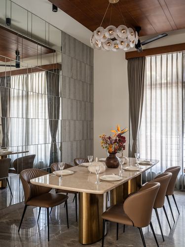 Dining room with marble-top brass-base table, leather chairs, mirrored wall, and floral chandelier