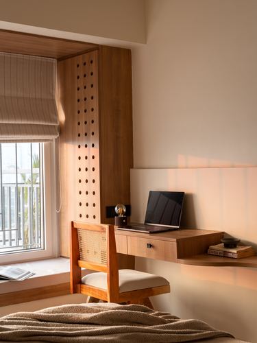 Sunlit study nook with floating wood desk, cane chair, and perforated wood panel by window
