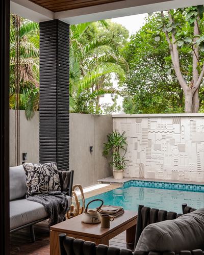 Covered patio with sofas overlooking a pool bordered by a textured relief wall and dense greenery.