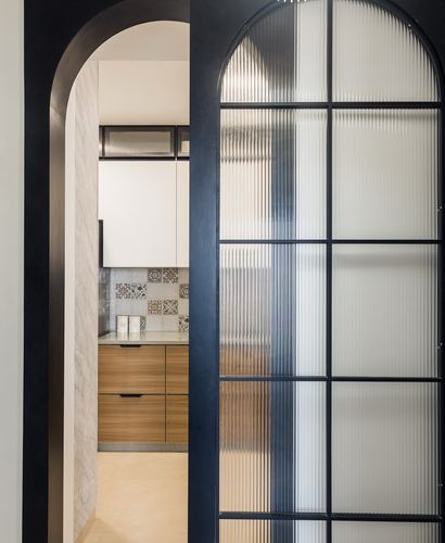 View through an arched fluted glass door into a kitchen with wood cabinetry and patterned tile backsplash
