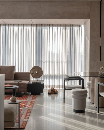 Neutral toned living room with terrazzo floor, sheer curtains, and sculptural stone decor object
