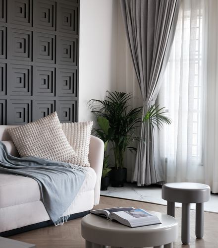 Living room corner with sculpted dark wall panel, beige sofa, sheer curtains and round stools